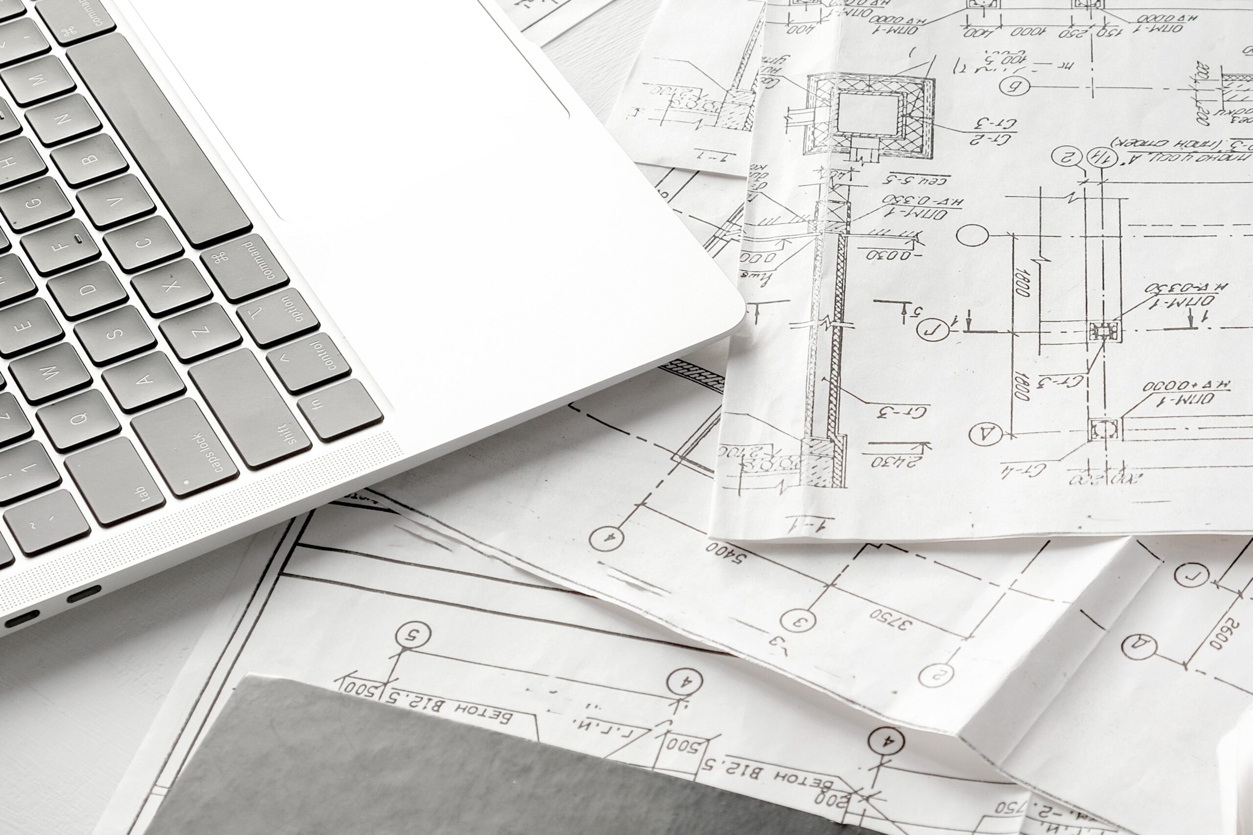 תכנון מבנים מסחריים על גבי שרטוטים אדריכליים לצד מחשב נייד במסגרת רישוי עסקים לחברות בנייה